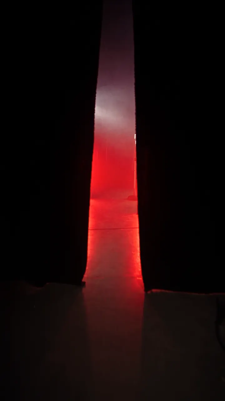 Between two black curtains, a gap: inside, the red light of the music set.