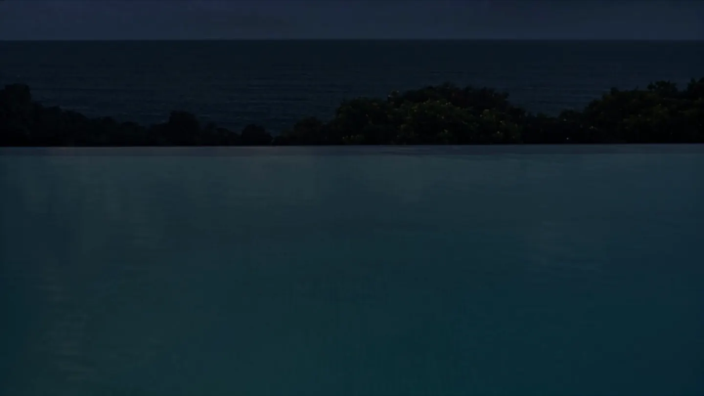 The still water of the infinity pool and, beyond its edge, the sea at night.